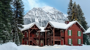 A log cabin with a porch and multiple windows, surrounded by snow and trees, with a mountain in the background. - Paradise Lodge & Bungalows (Lake Louise)