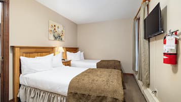 A hotel room with two beds, a television, a fire extinguisher, and a painting on the wall.