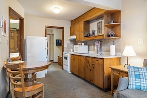 A compact kitchen with wooden cabinets, a white refrigerator, a microwave, and a coffee maker.