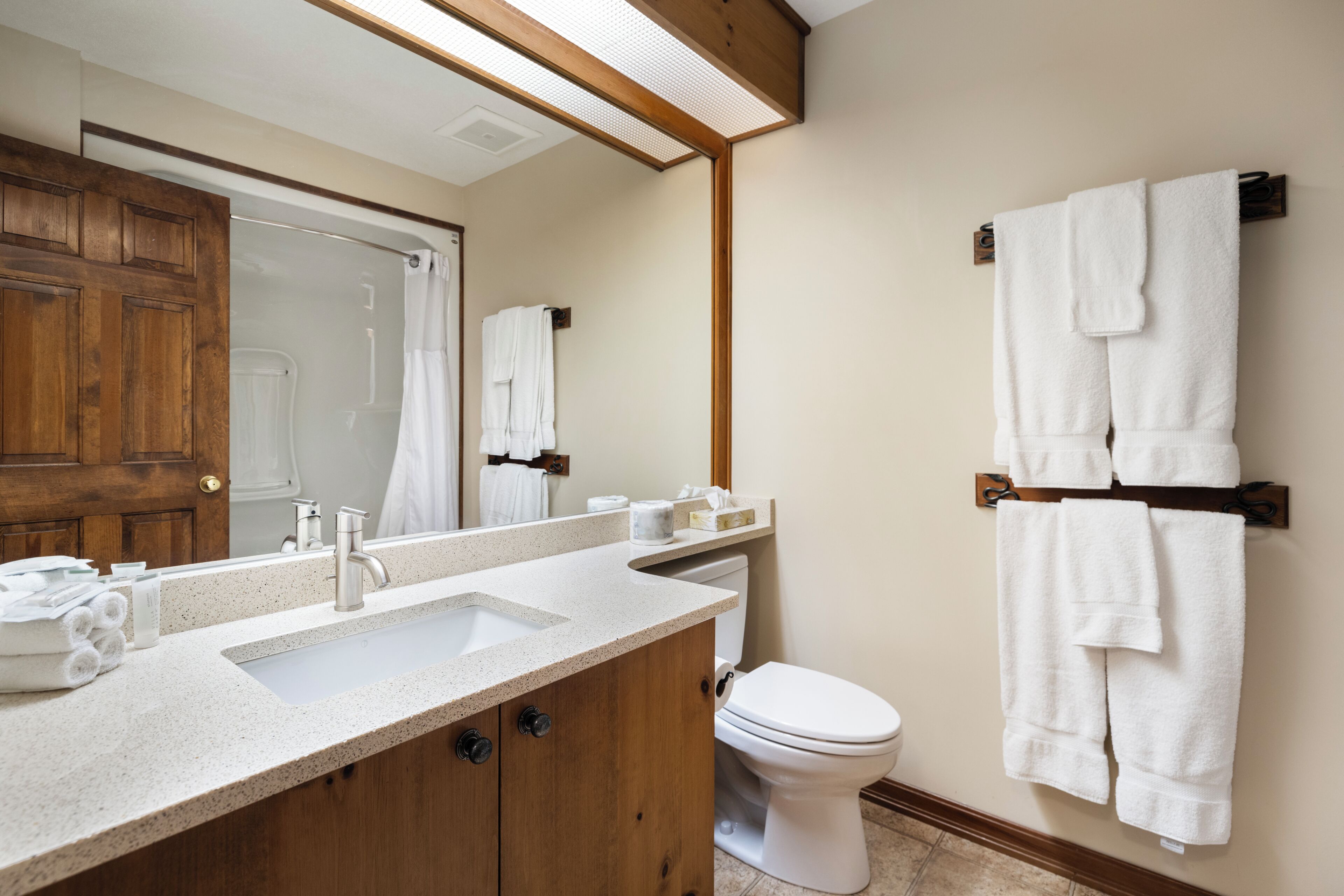 Een badkamer met een houten wastafel, een witte wasbak, een toilet en een handdoekrek met meerdere handdoeken.