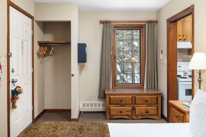 Um quarto com um banco de madeira, um radiador, uma janela com cortinas, um porta-roupas e uma porta com um brinquedo macio.