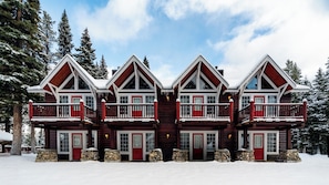 A symmetrical, multi-story log cabin with a central staircase, surrounded by snow-covered trees. - Paradise Lodge & Bungalows (Lake Louise)