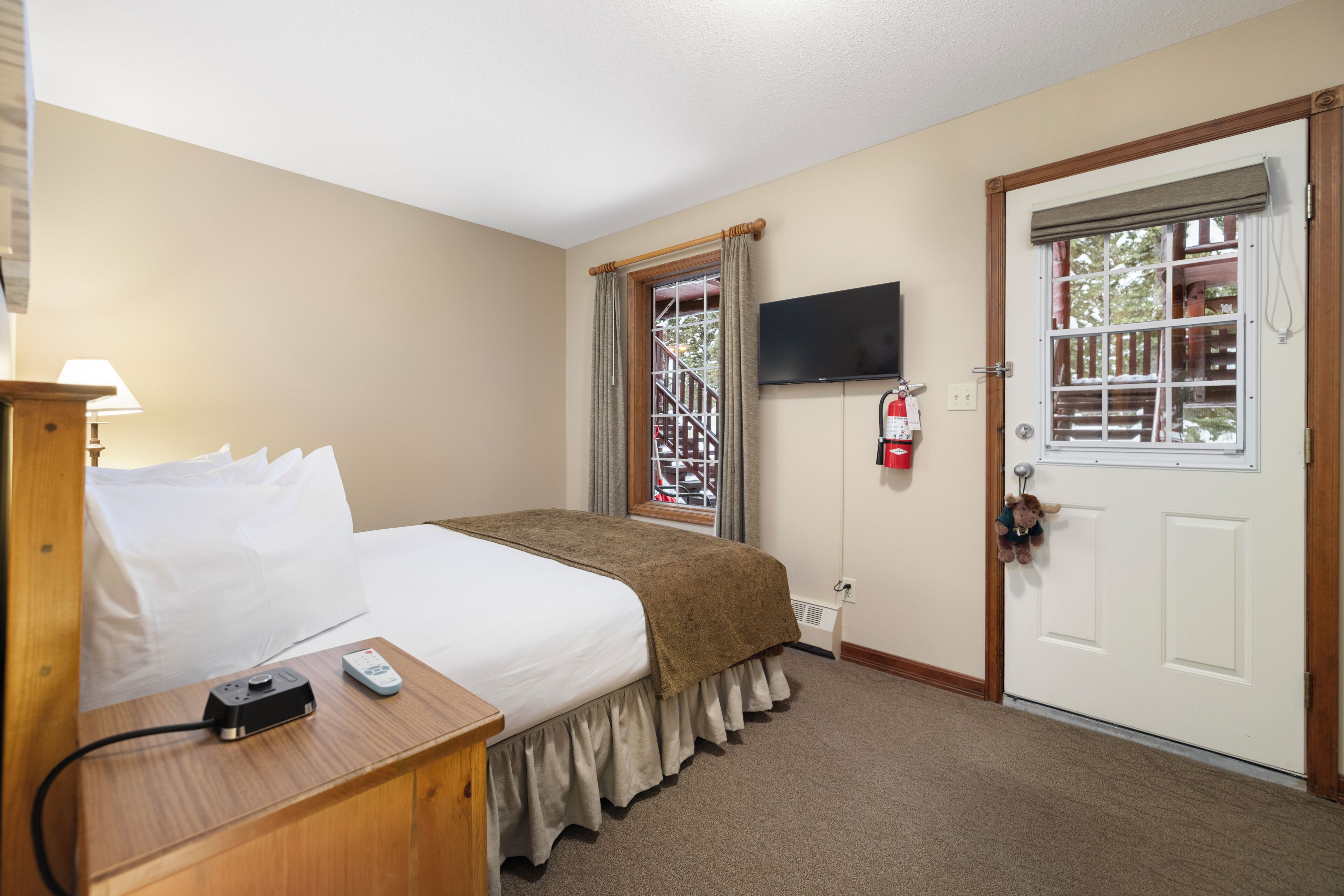 Une chambre d’hôtel comprenant un lit, une table de chevet, une lampe, une télévision et une porte avec une fenêtre.