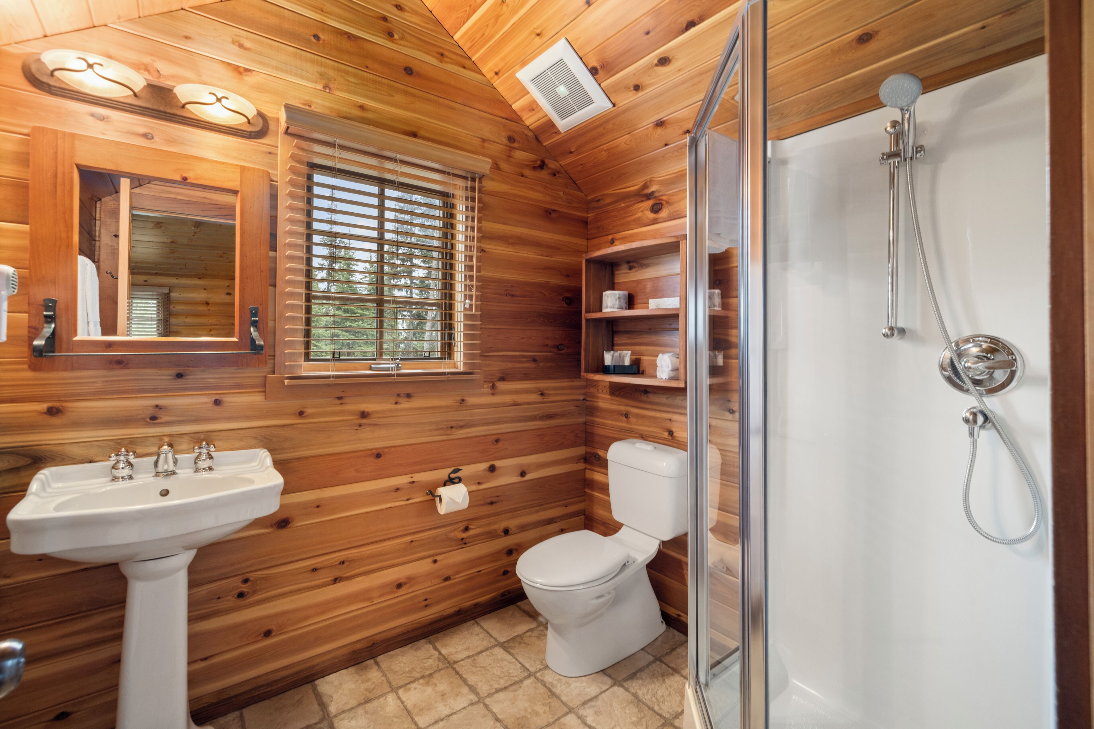 A wooden cabin bathroom with a sink, toilet, and shower.