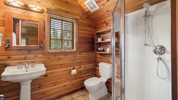 Un baño rústico con cabina de ducha, lavabo e inodoro.