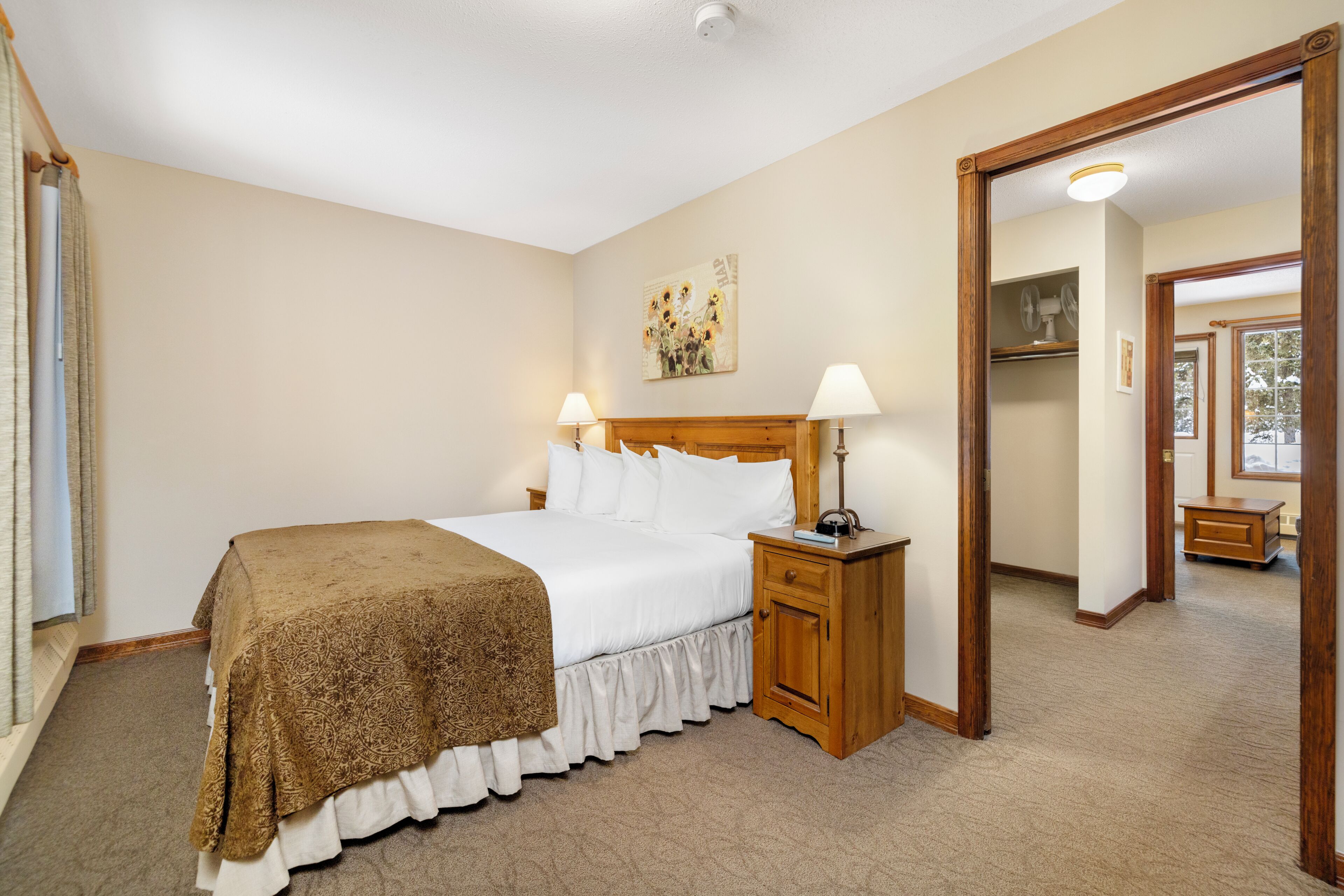 A hotel room with a bed, bedside lamps, a nightstand, a mirror, and a door leading to another room.