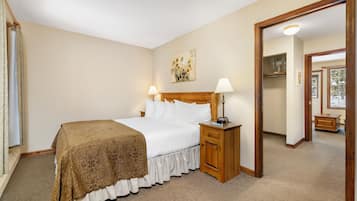 A hotel room with a bed, bedside lamps, a nightstand, a mirror, and a door leading to another room.