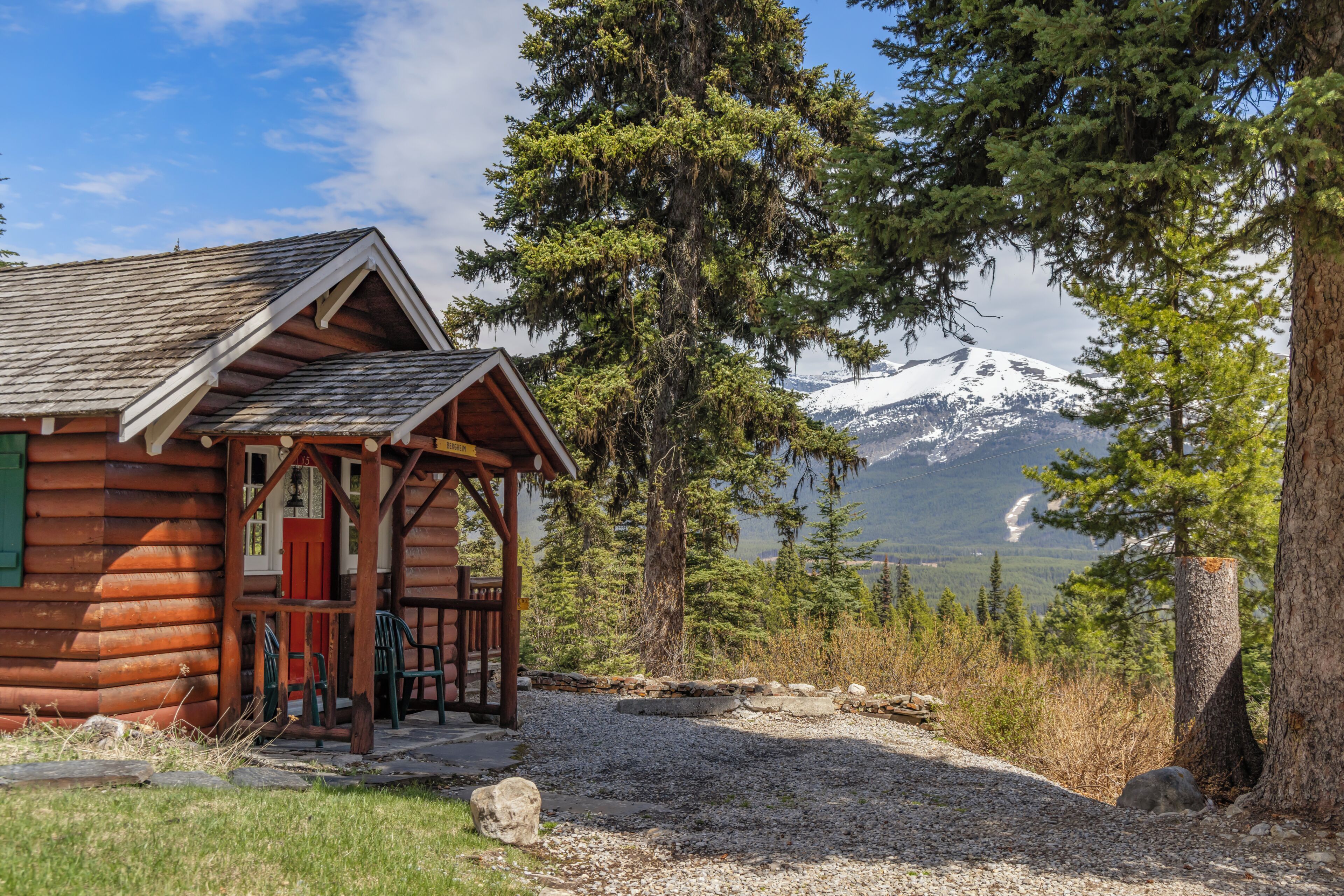 A log cabin with a porch, a red door, and a view of a snow-capped mountain.