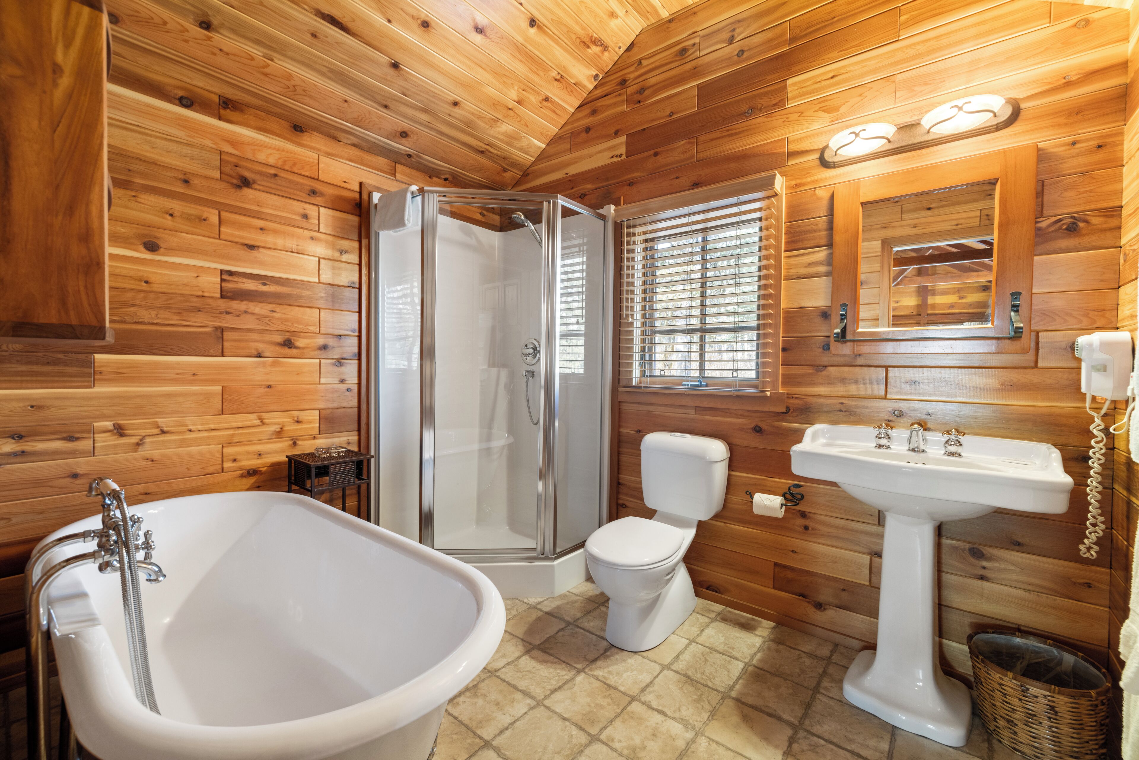 Een houten badkamer in een vakantiehuis, met een douche, toilet, wastafel en een groot bad.