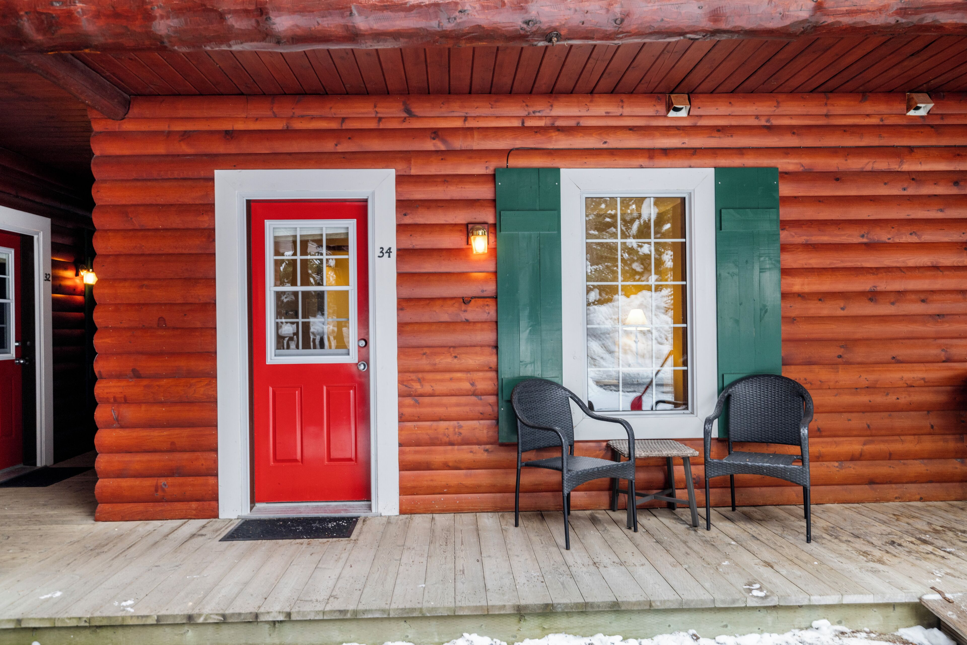 A wooden cabin with a red door, numbered 34, and two chairs on a wooden deck.