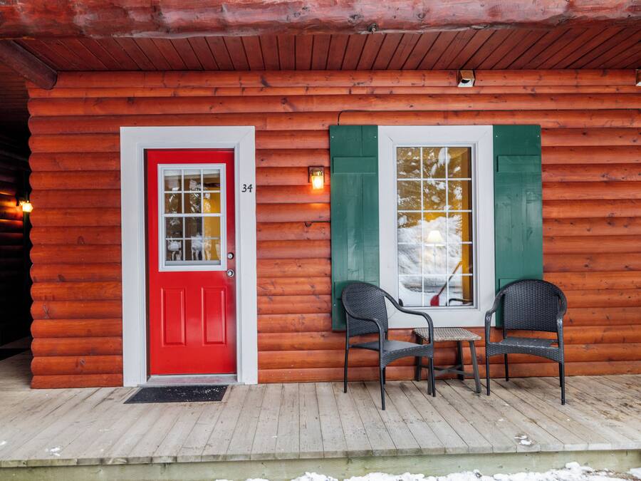 A wooden cabin with a red door, numbered 34, and two chairs on a wooden deck.