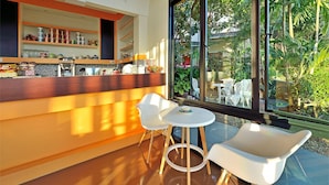 Eine moderne Bar mit Holztresen, weißen Stühlen und einem großen Fenster mit Blick auf üppiges Grün.