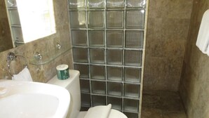 Un baño con cabina de ducha de vidrio, inodoro y lavamanos.