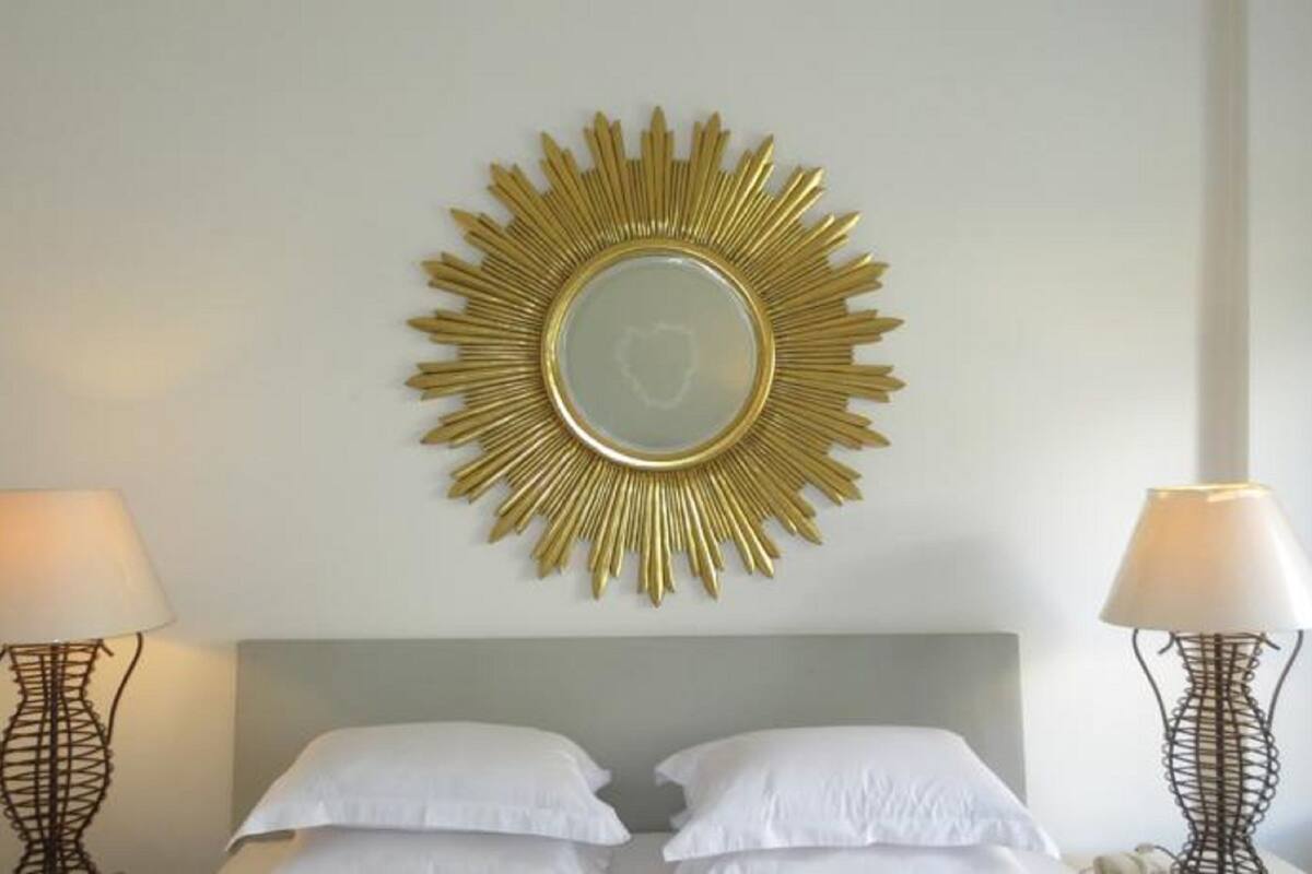 A hotel room with a bed, two bedside lamps, and a sunburst mirror on the wall.