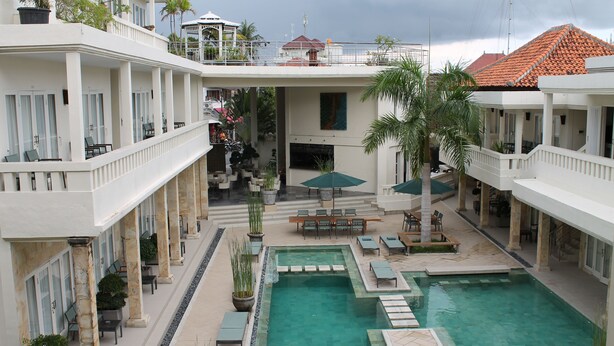 Un hotel con piscina central, mobiliario exterior y varios balcones.