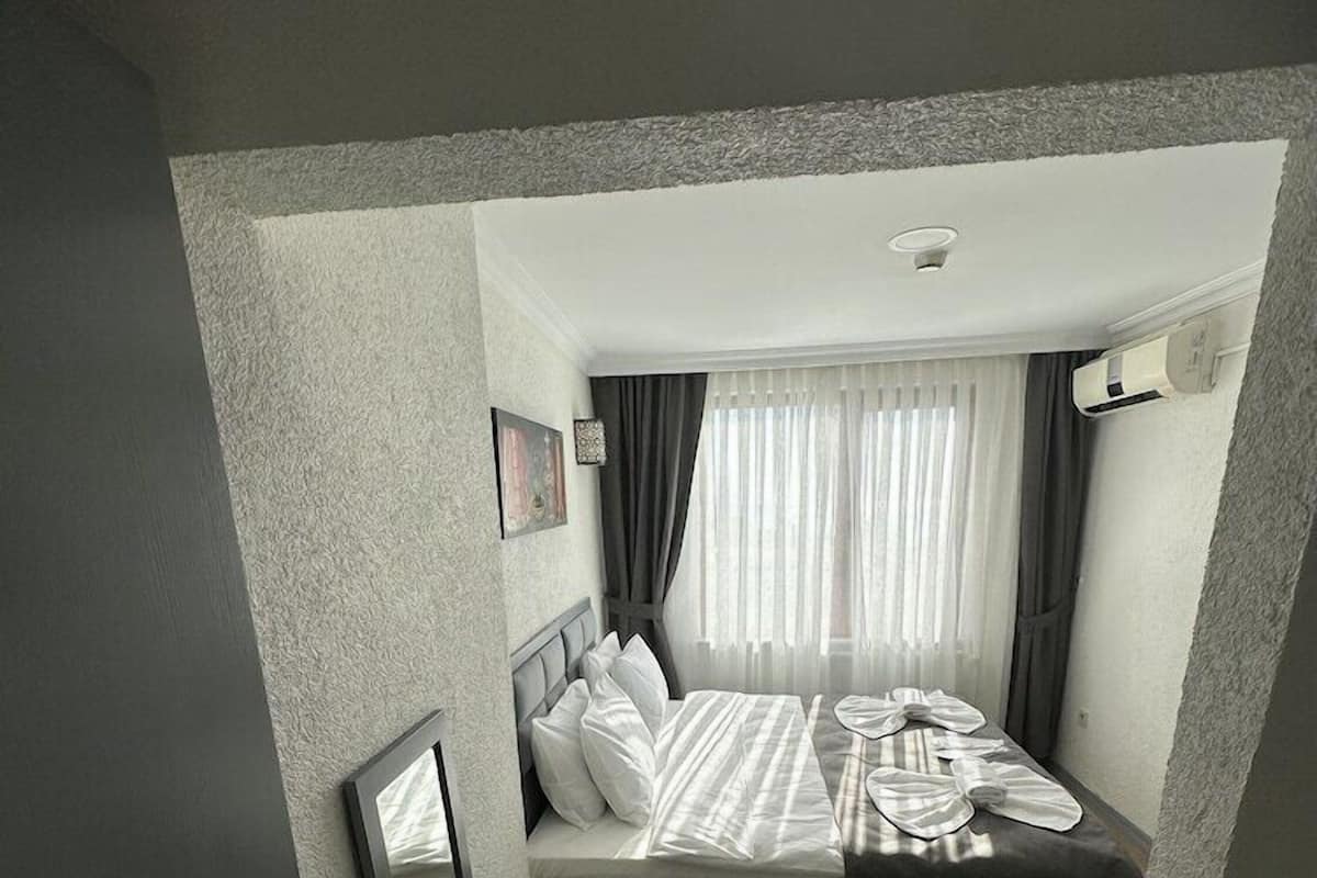 A compact hotel room with a bed, a desk, a chair, a TV, and a window with curtains.