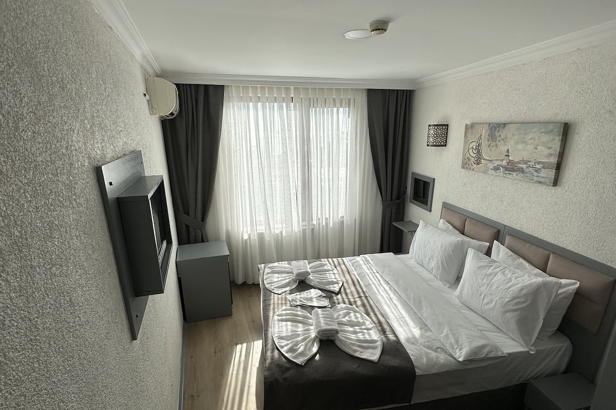 A hotel room with a large bed, a bedside table, a TV, and a painting on the wall.