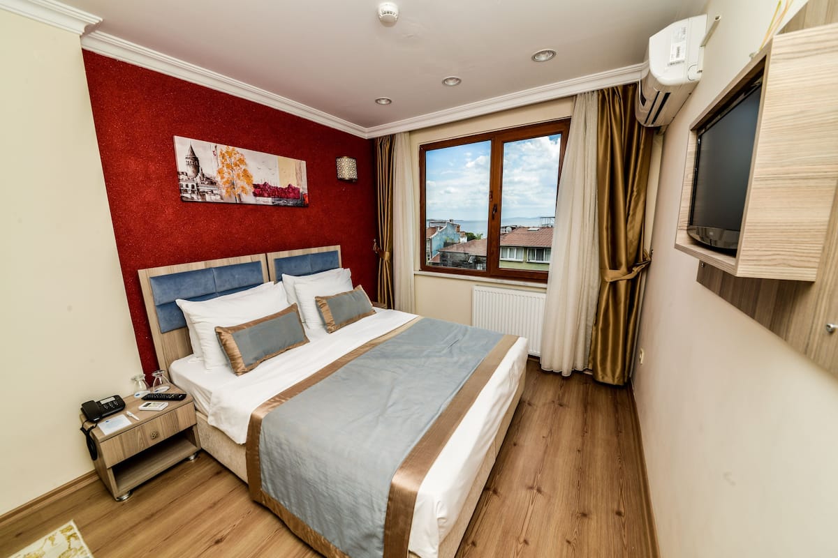A hotel room with a bed, a nightstand, a window with curtains, and a wall-mounted TV.
