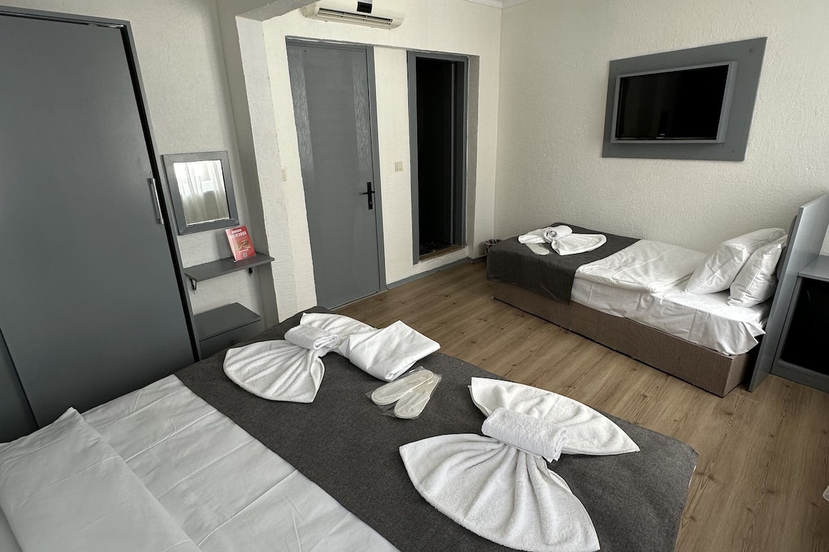 A hotel room with a bed, a sofa bed, a TV mounted on the wall, and a door leading to a bathroom.
