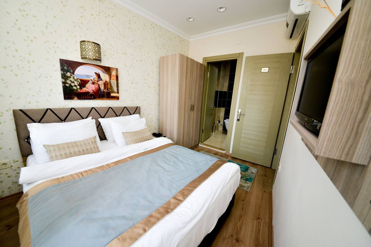 A bedroom with a bed, a television, a wardrobe, and a door leading to another room.