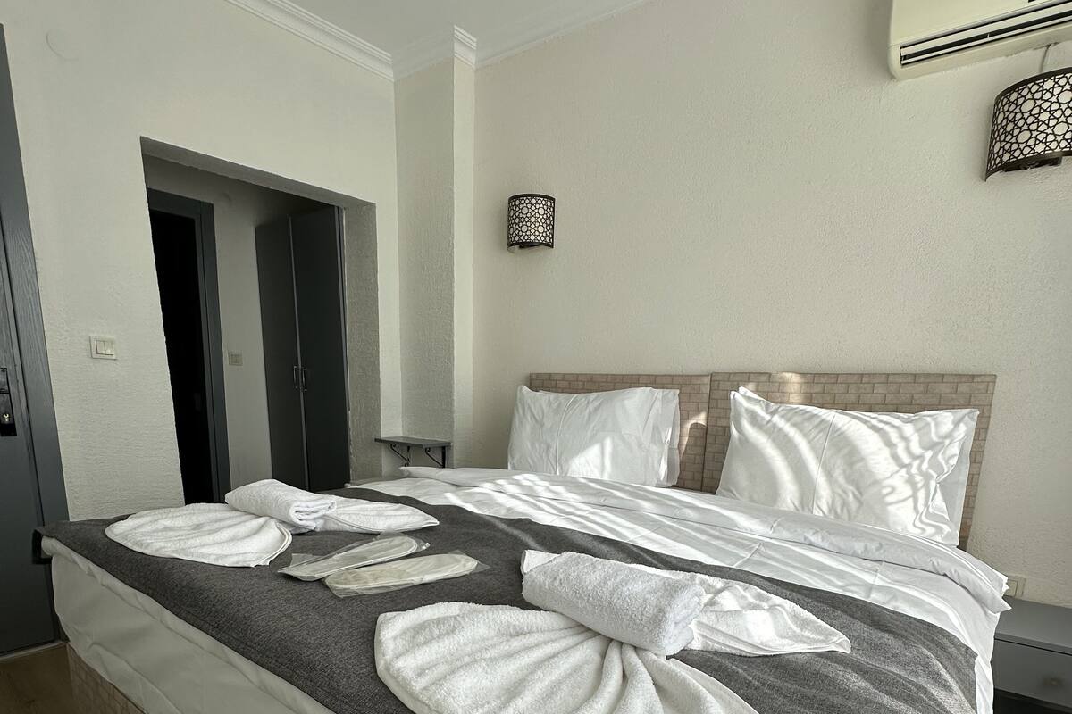 A neatly made bed with white linens and towels, a headboard, and a wall-mounted air conditioner.