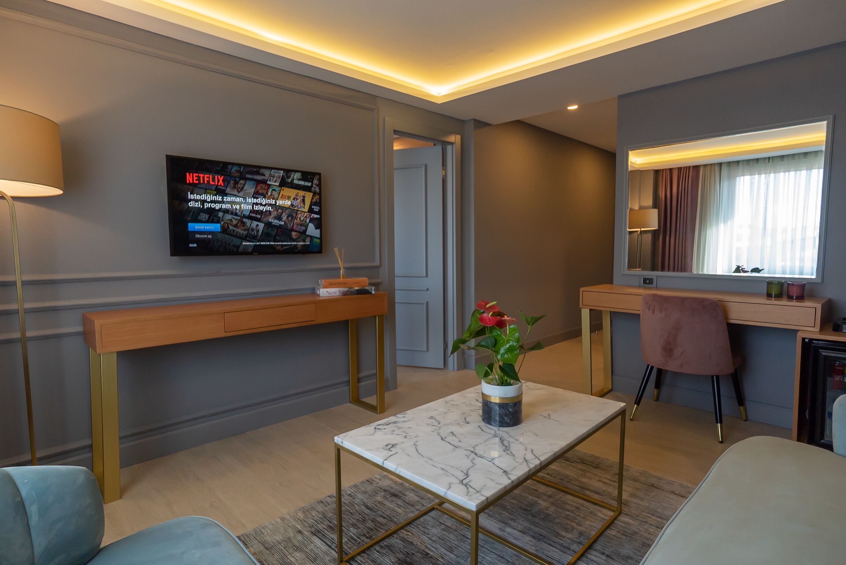 A modern hotel room with a TV displaying Netflix content, a wooden desk, a marble coffee table, and a comfortable seating area.