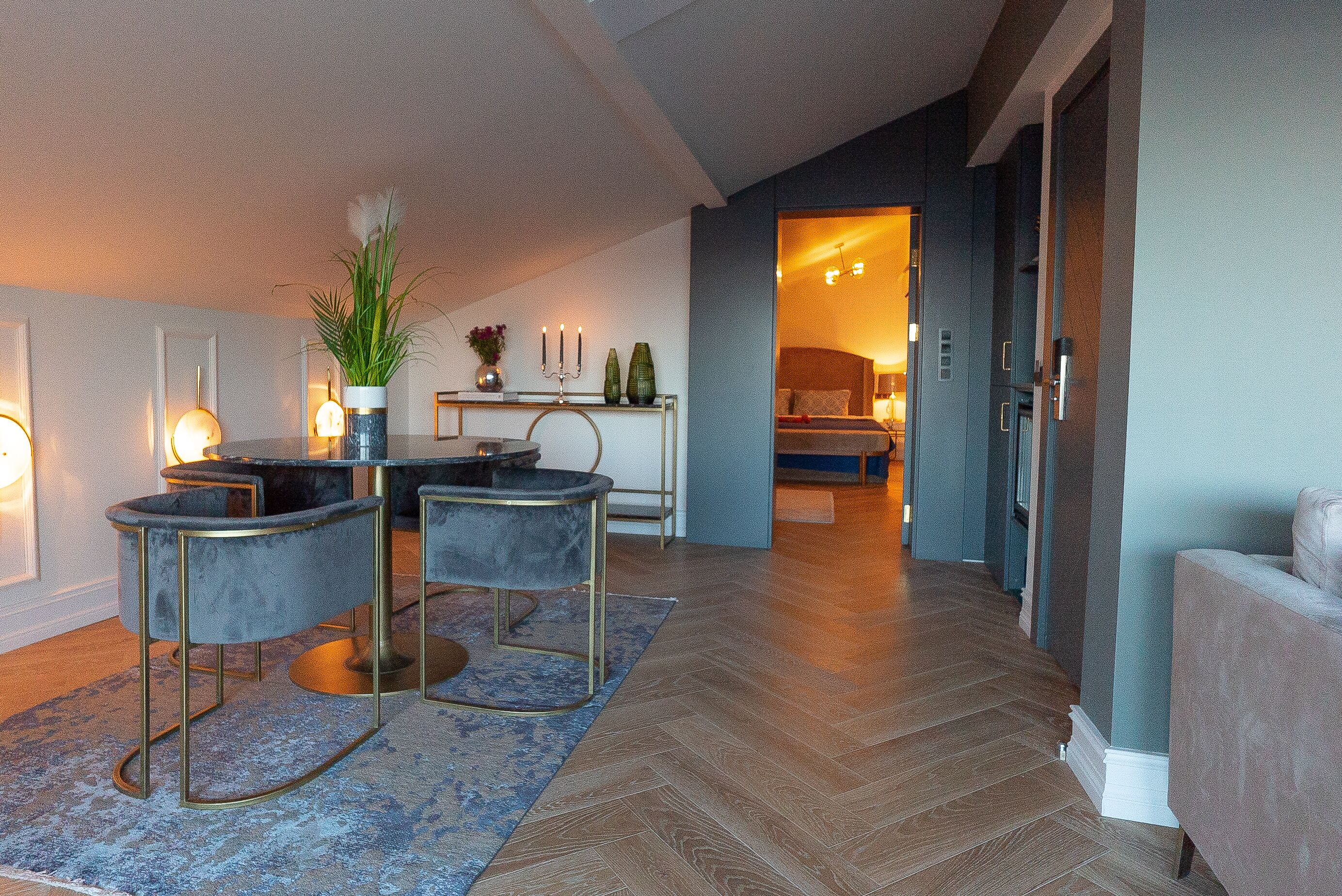 A modern living room with a herringbone wood floor, a blue rug, and a dining area with a table and chairs.