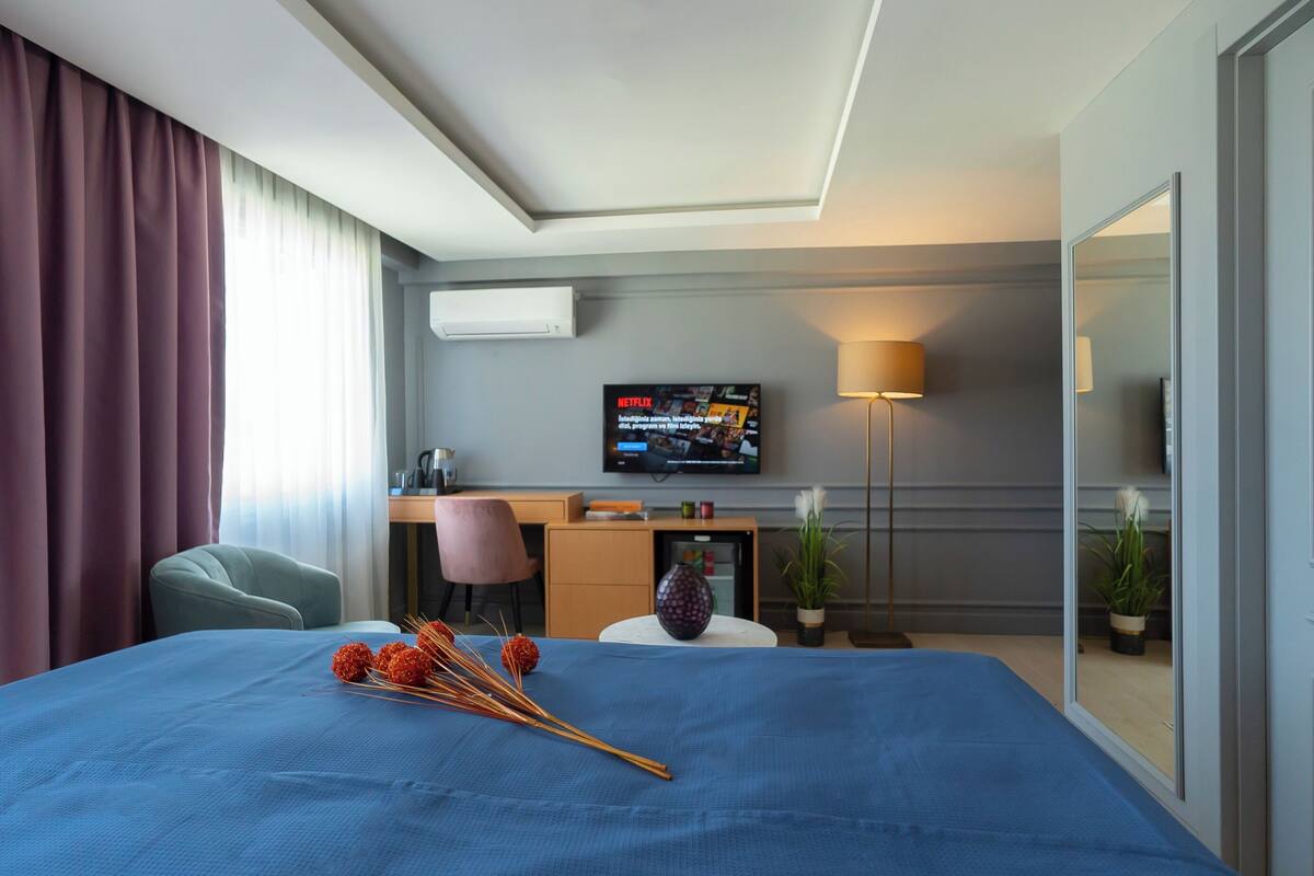 Habitación de hotel con cama, escritorio, televisión, lámpara y espejo.