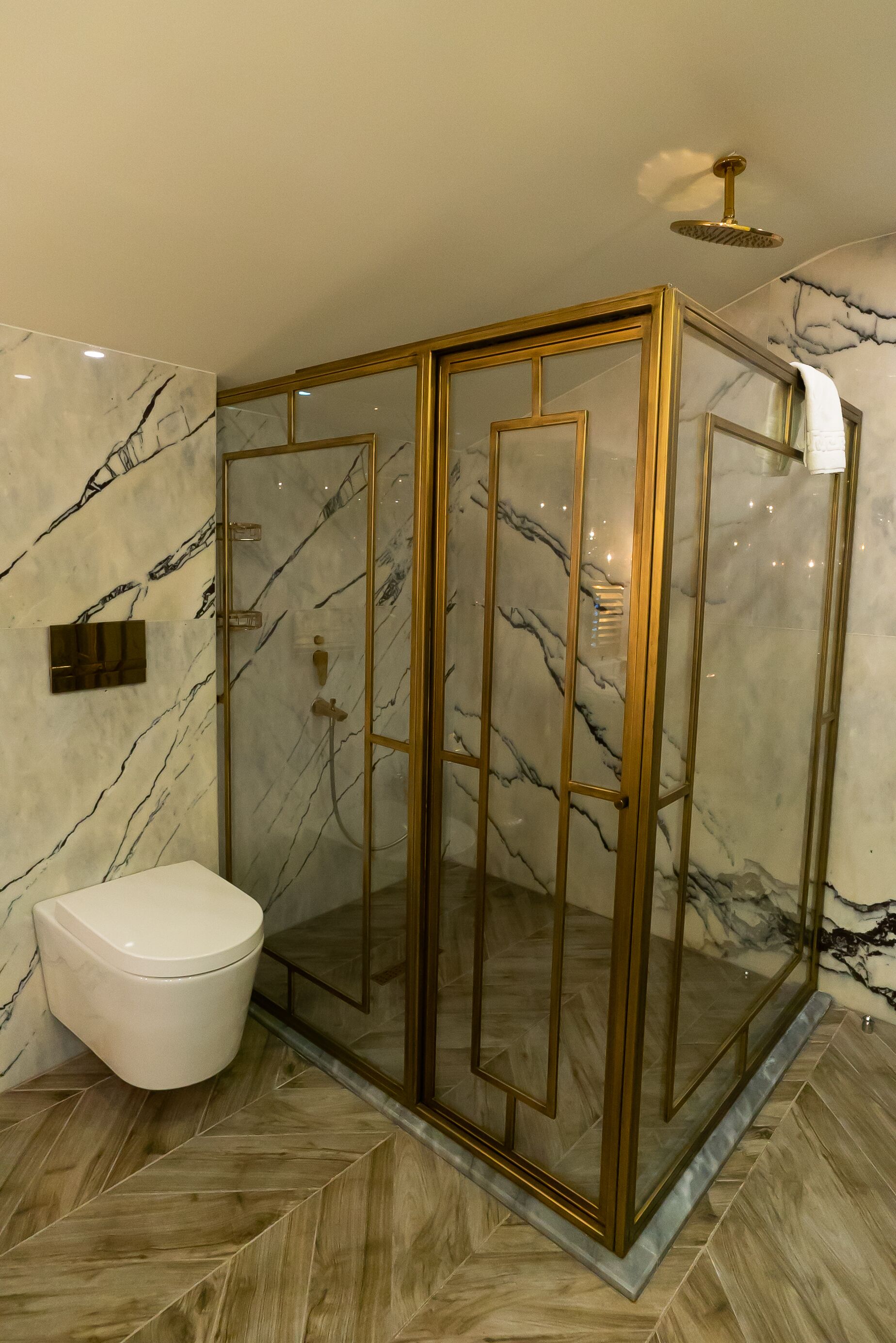 A modern bathroom with a glass-enclosed shower, marble walls, and a herringbone-patterned floor.