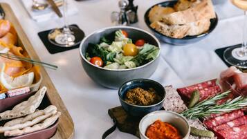 Una mesa de comedor con diferentes alimentos, como pan, carnes y ensaladas, junto con copas de vino.