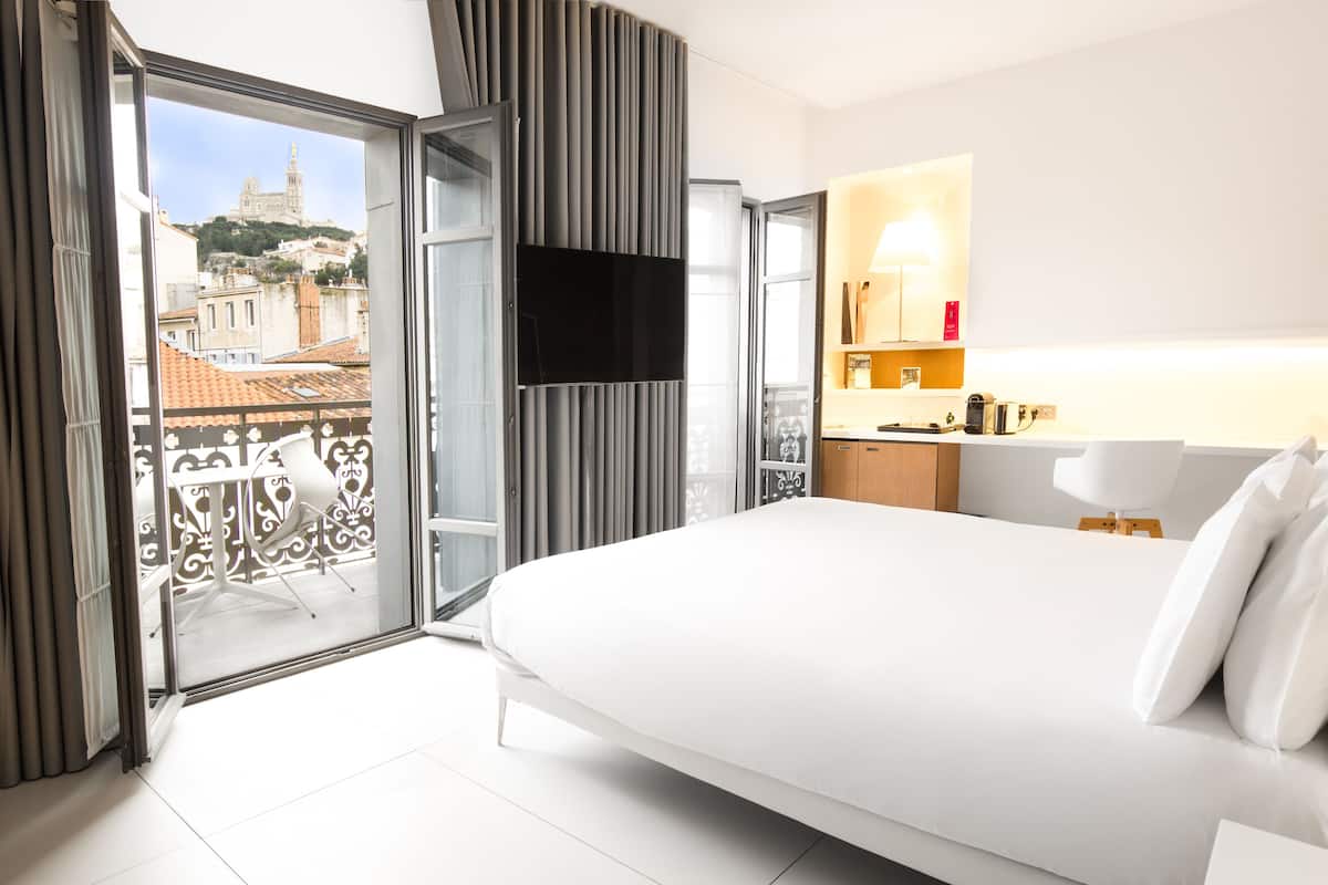 Une chambre d’hôtel comprenant un lit, une télévision, un balcon avec vue sur la ville et une petite kitchenette.