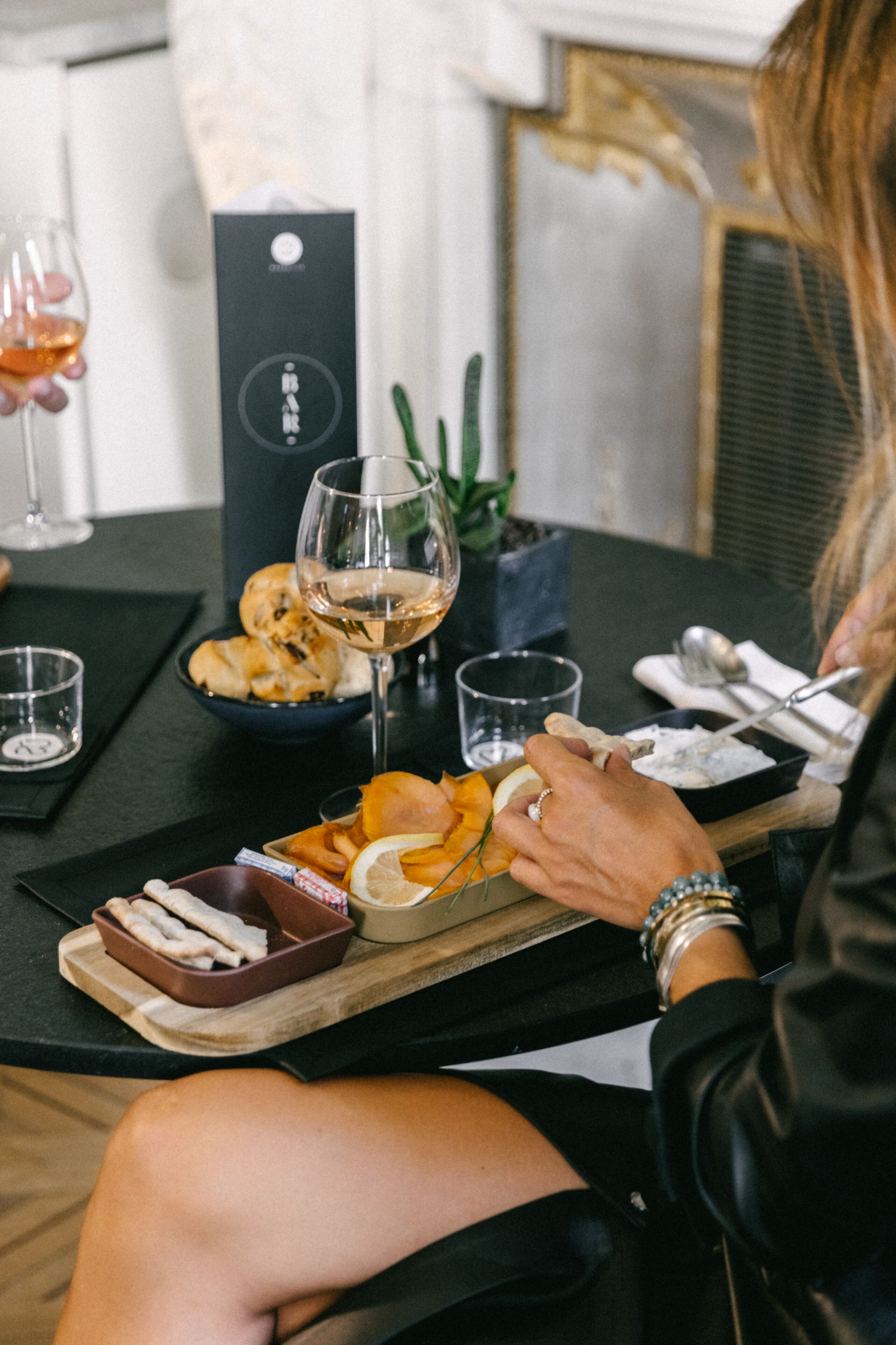A dining table with a glass of wine, a bowl of bread, and a plate of snacks.