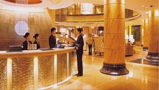 Un vestíbulo de hotel con mostrador de recepción, amplias columnas y un techo alto.
