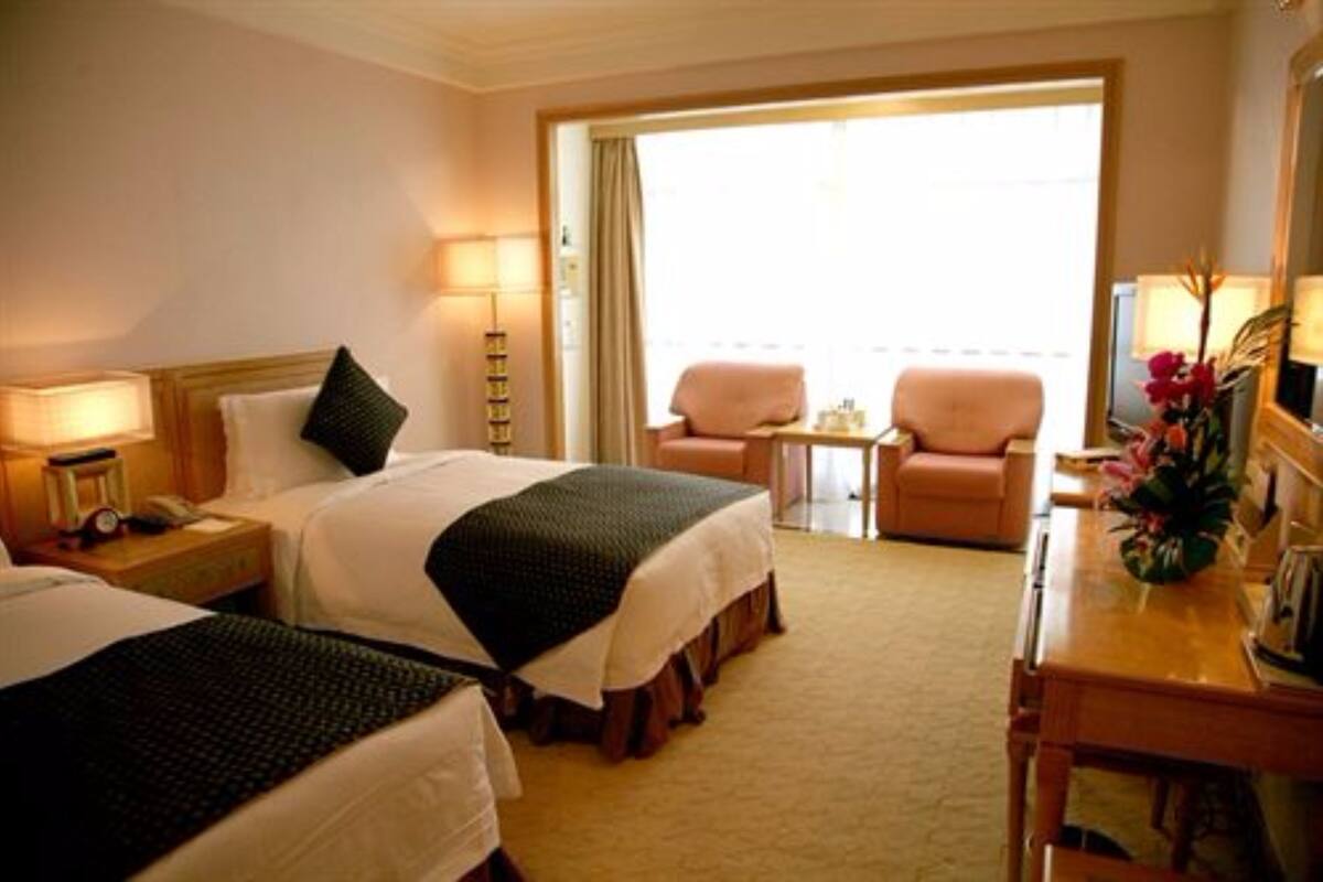 Ein Hotelzimmer mit zwei Betten, einem Schreibtisch, einem Stuhl, einem kleinen Tisch und einem Balkon mit Sitzgelegenheit.