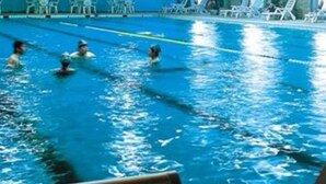 Una piscina interior con carriles de natación, sillas de descanso y un techo con estructura de cerchas.