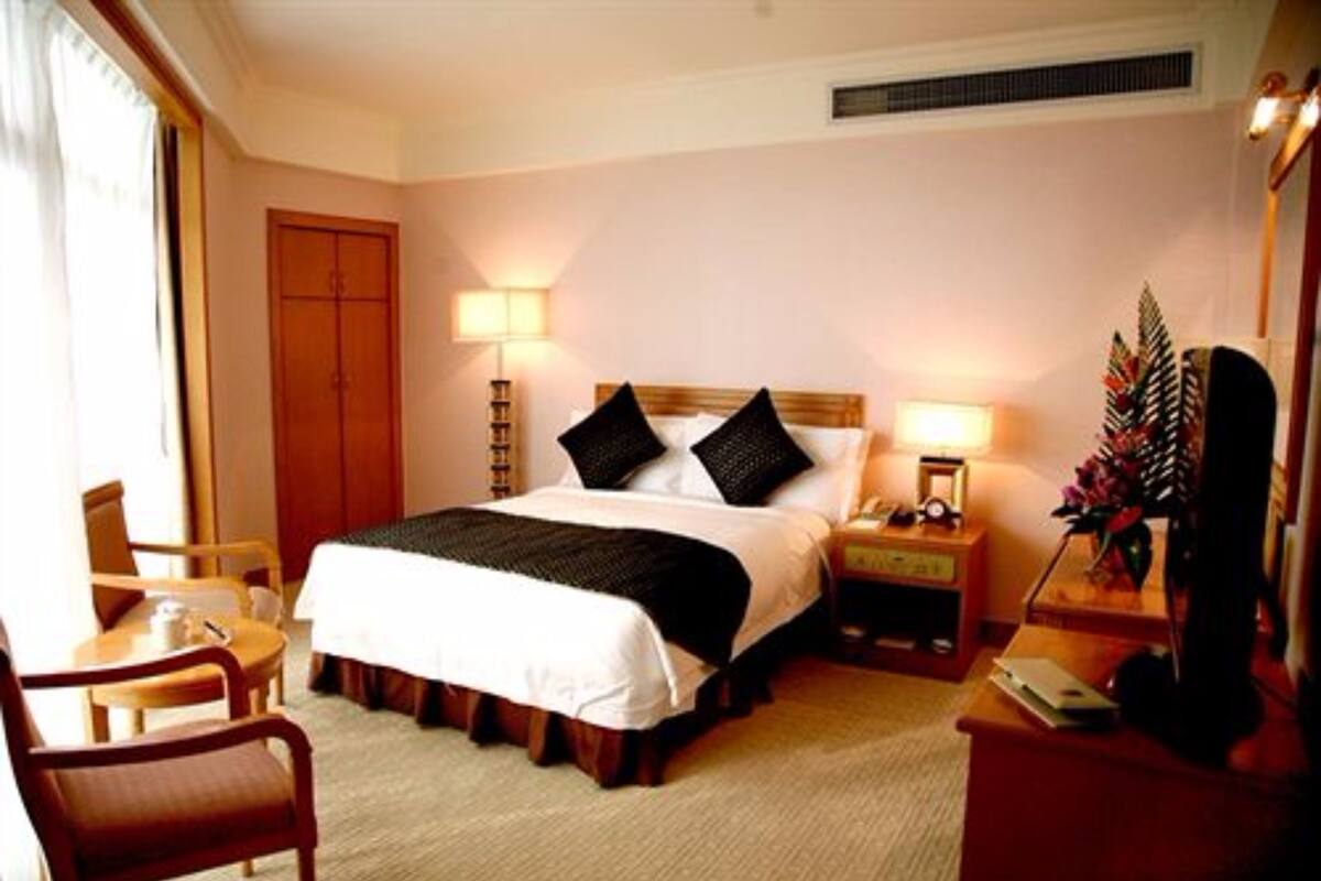 Ein Hotelzimmer mit Bett, Nachttisch, Lampe, Stuhl und Schreibtisch mit Computer.