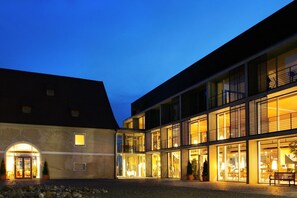 A modern building with multiple levels, large windows, and a courtyard with a paved area and potted plants. - Waldsee Golf Resort (Bad Waldsee)