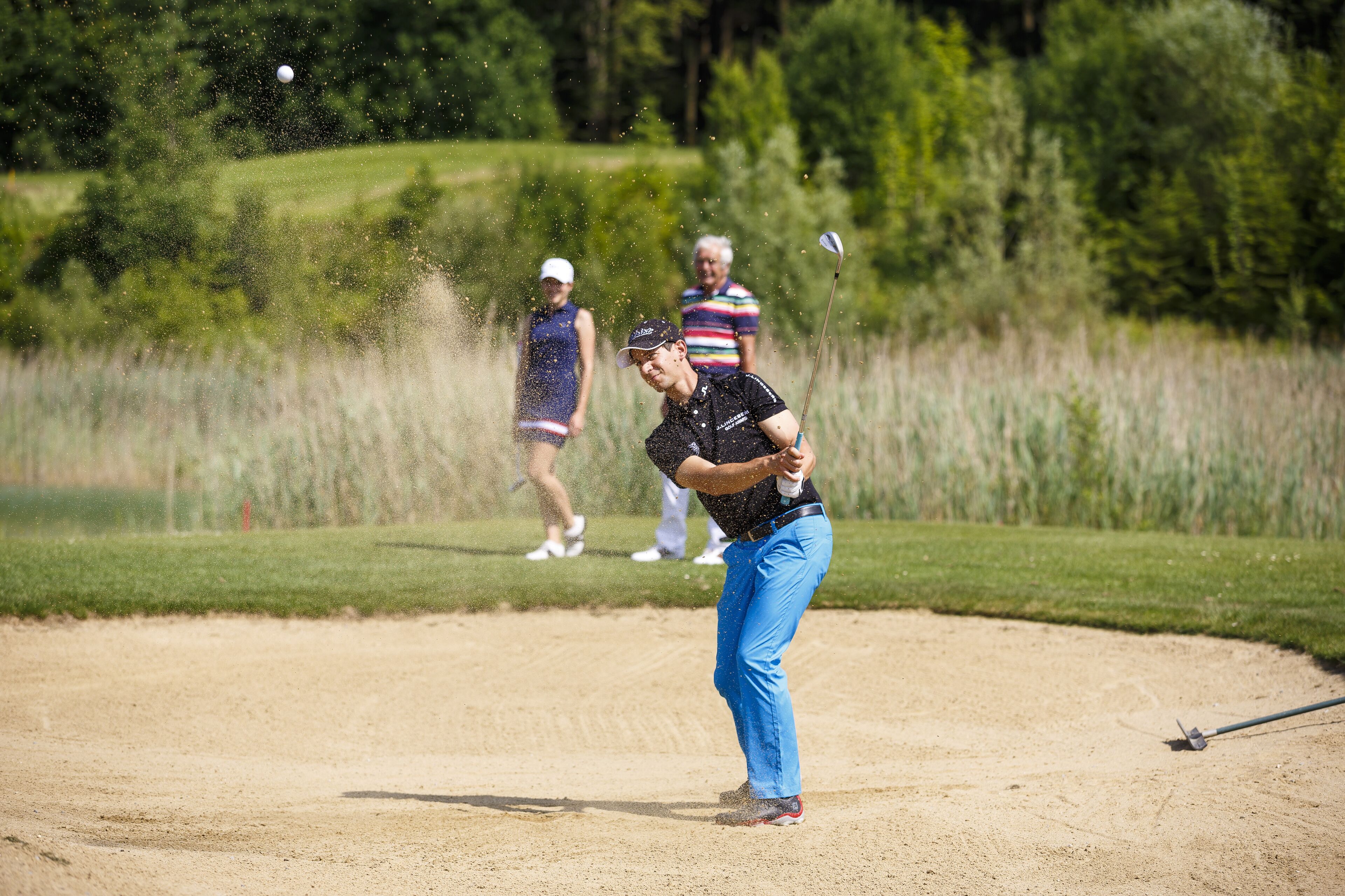 Un parcours de golf avec un bunker de sable, un green d’entraînement et une zone boisée en arrière-plan.