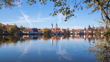 Ein ruhiger See spiegelt Gebäude und Bäume wider, mit blauem Himmel.