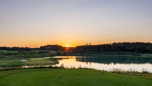 Een golfbaan bij zonsondergang met een meer, bomen en een heldere lucht.