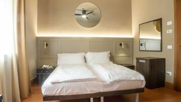 A hotel room with a bed, bedside tables, a mirror, and a clock on the wall.