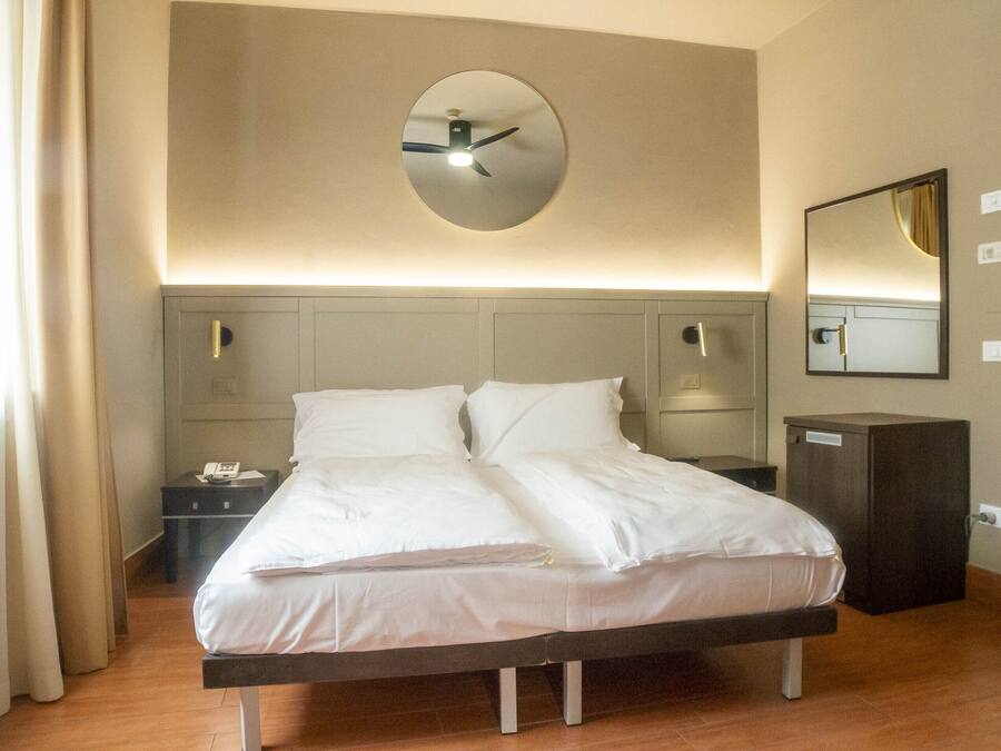A hotel room with a bed, bedside tables, a mirror, and a clock on the wall.