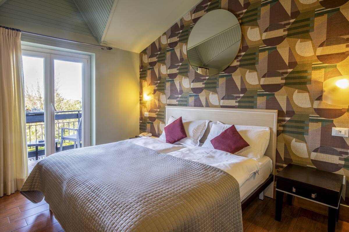 A bedroom with a bed, a nightstand, a mirror, and a patterned wall.