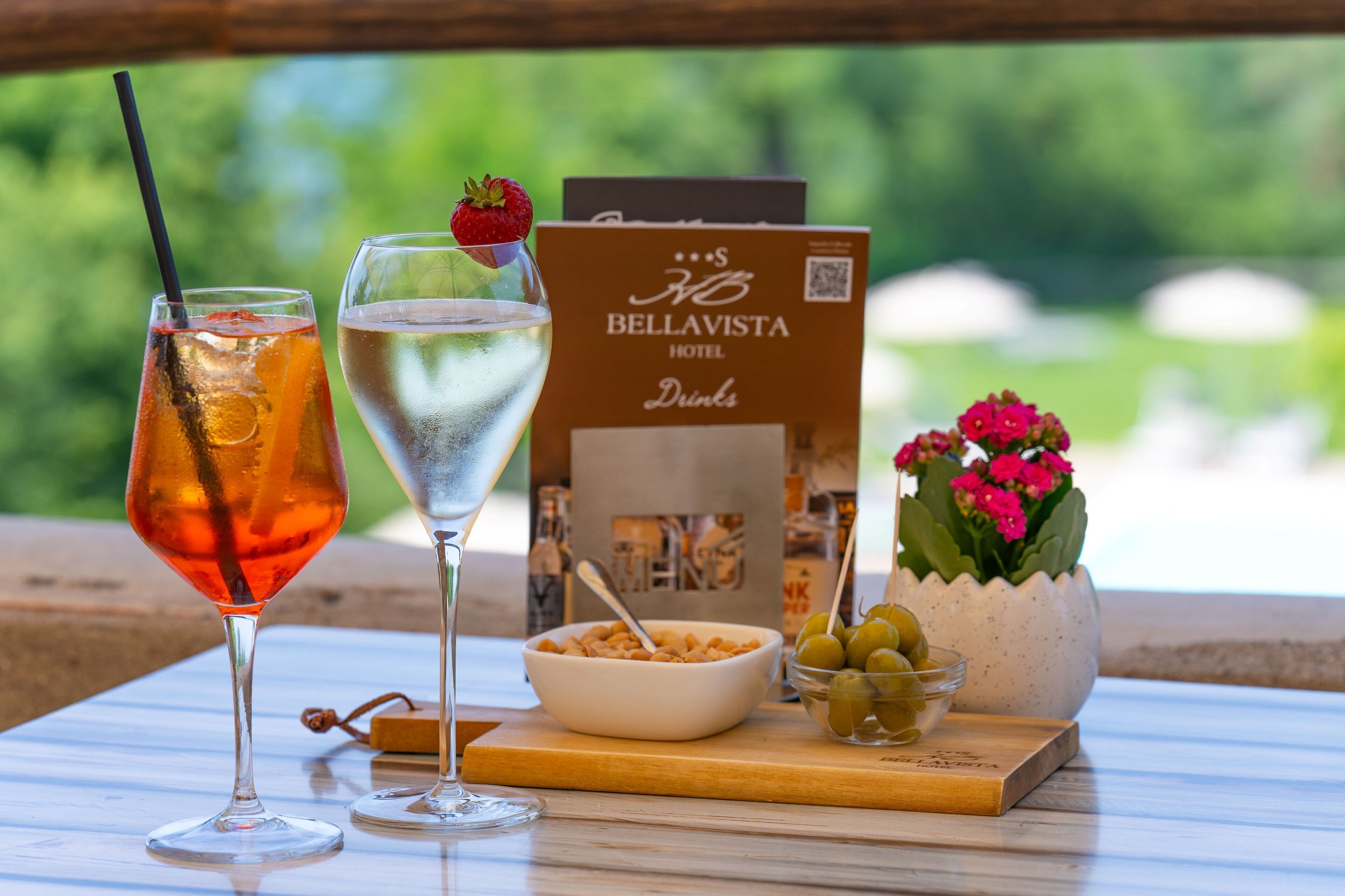 Two drinks on a table with a Bellavista Hotel sign, a bowl of cereal, and a potted plant.