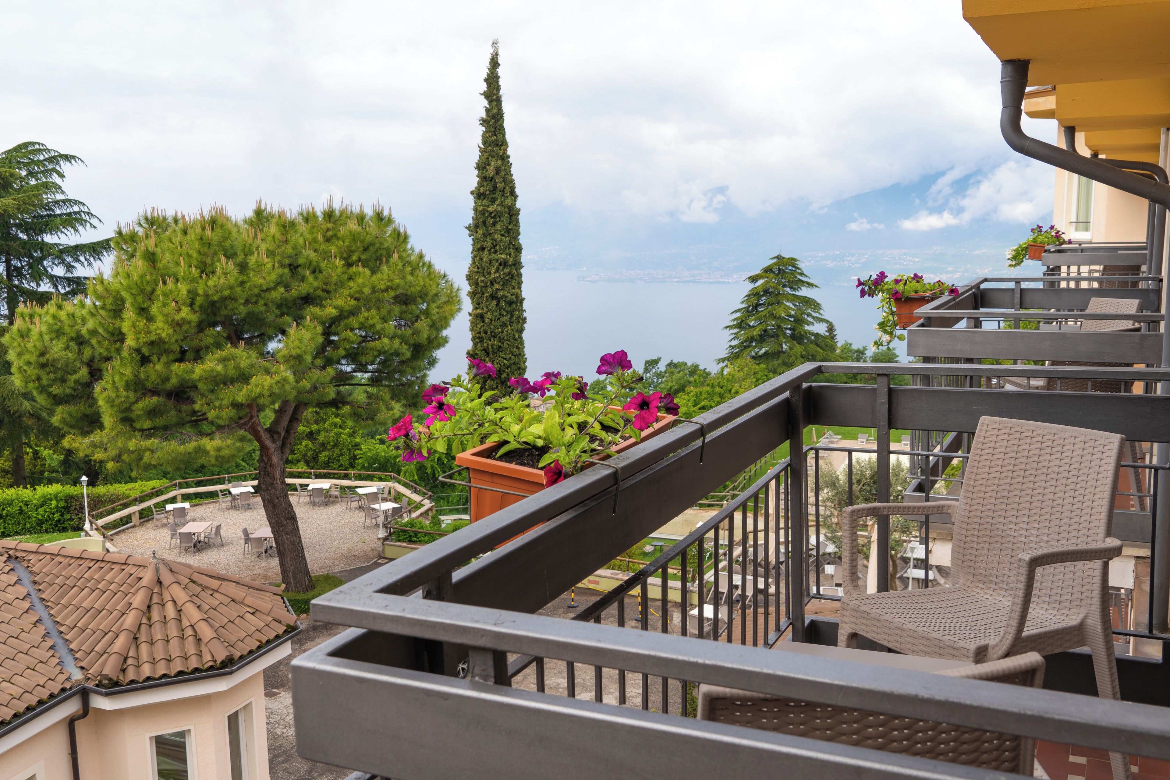 Ein Balkon mit Korbstuhl, Blument öpfen mit Blumen und Blick auf Bäume und eine entfernte Landschaft.