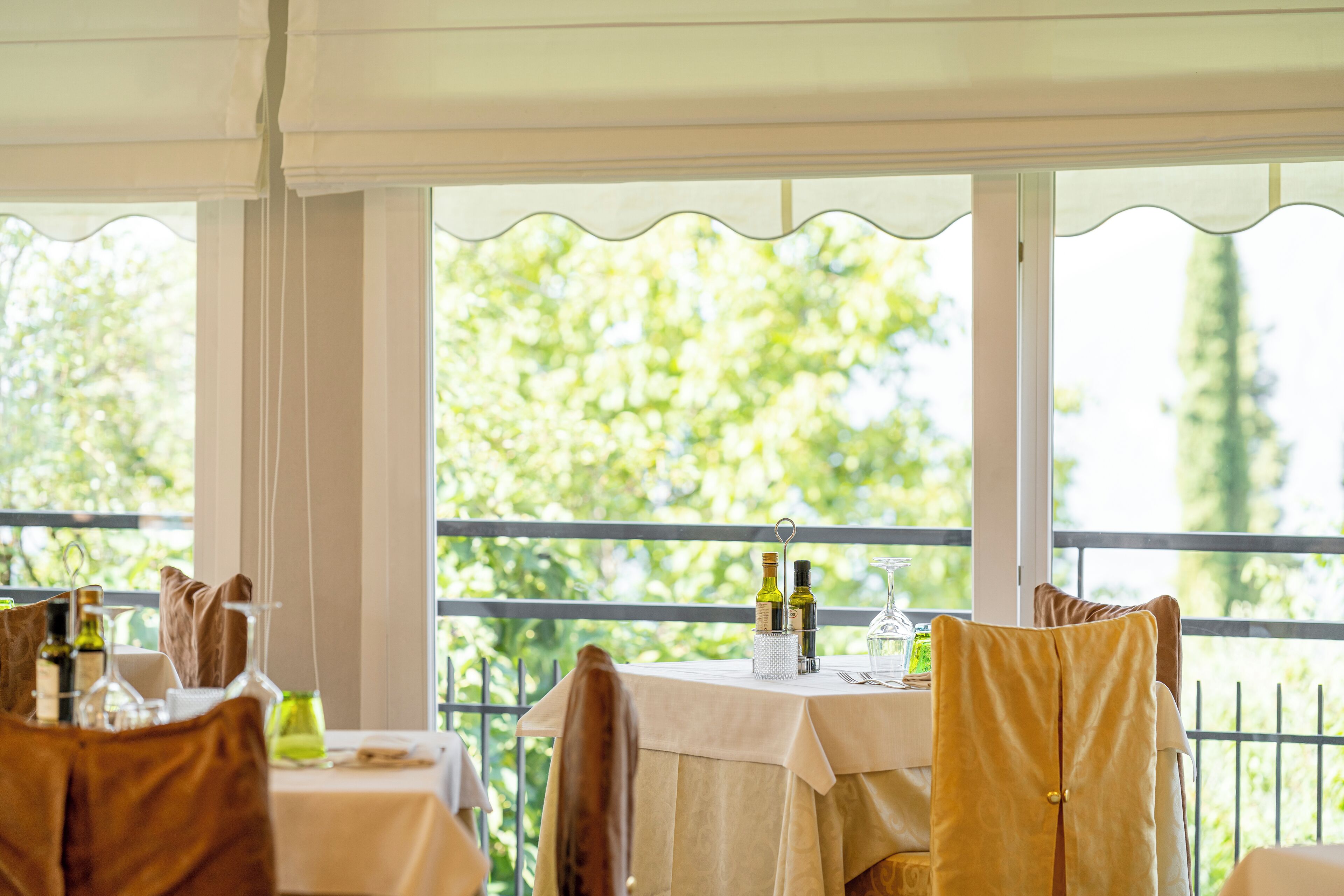 Un espace repas avec des tables préparées pour deux personnes, offrant une vue sur la verdure grâce à de grandes fenêtres.