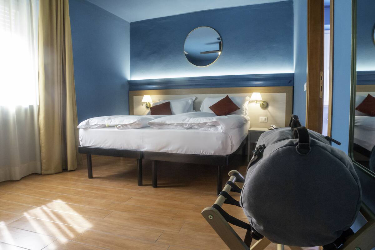 Habitación de hotel con una cama grande, dos mesitas de noche con lámparas, un espejo redondo en la pared y suelo de madera.