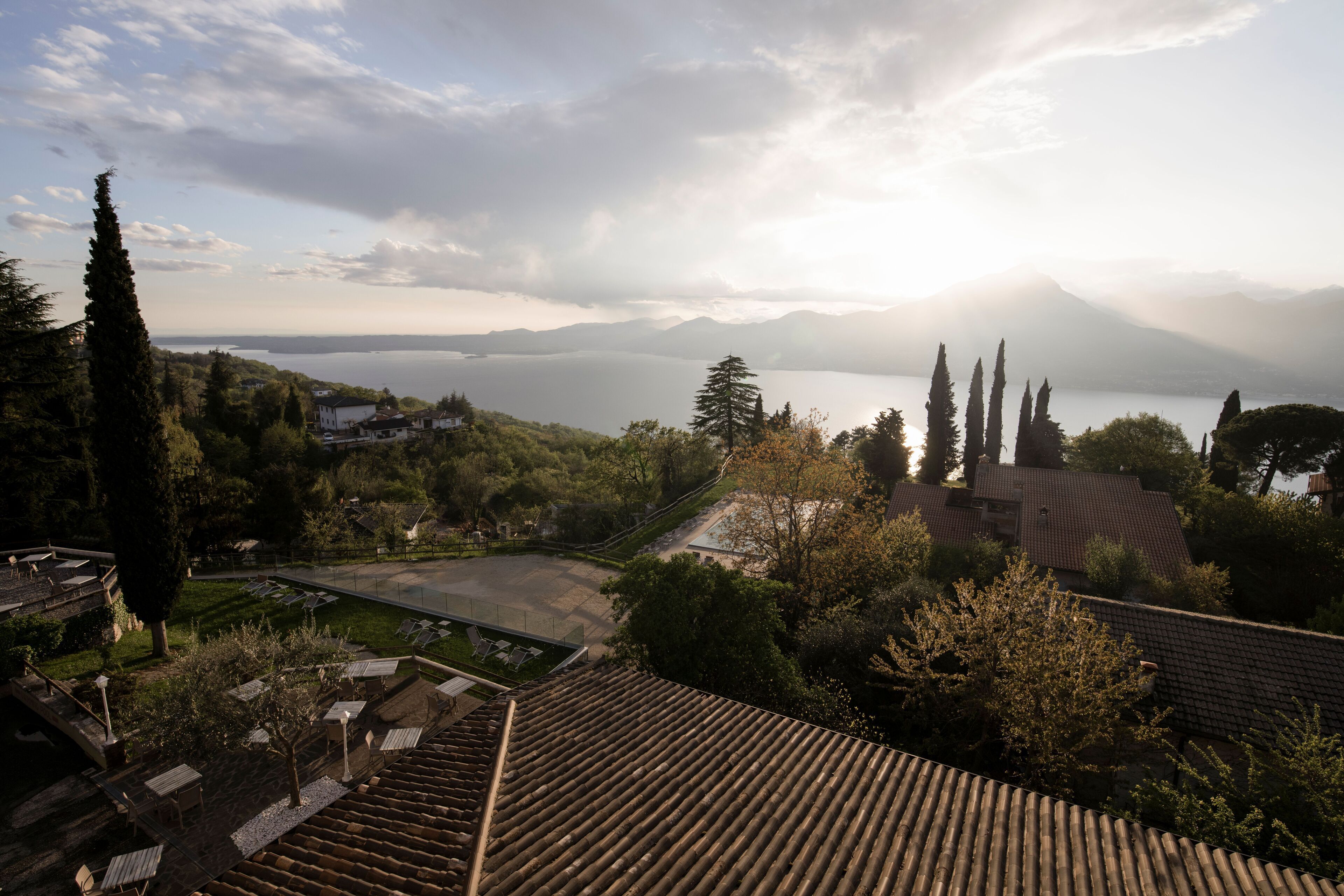 Ein Panoramablick auf ein Resort mit terrassenförmigen Sitzgelegenheiten, einem Pool und einem malerischen See mit Bergen im Hintergrund.