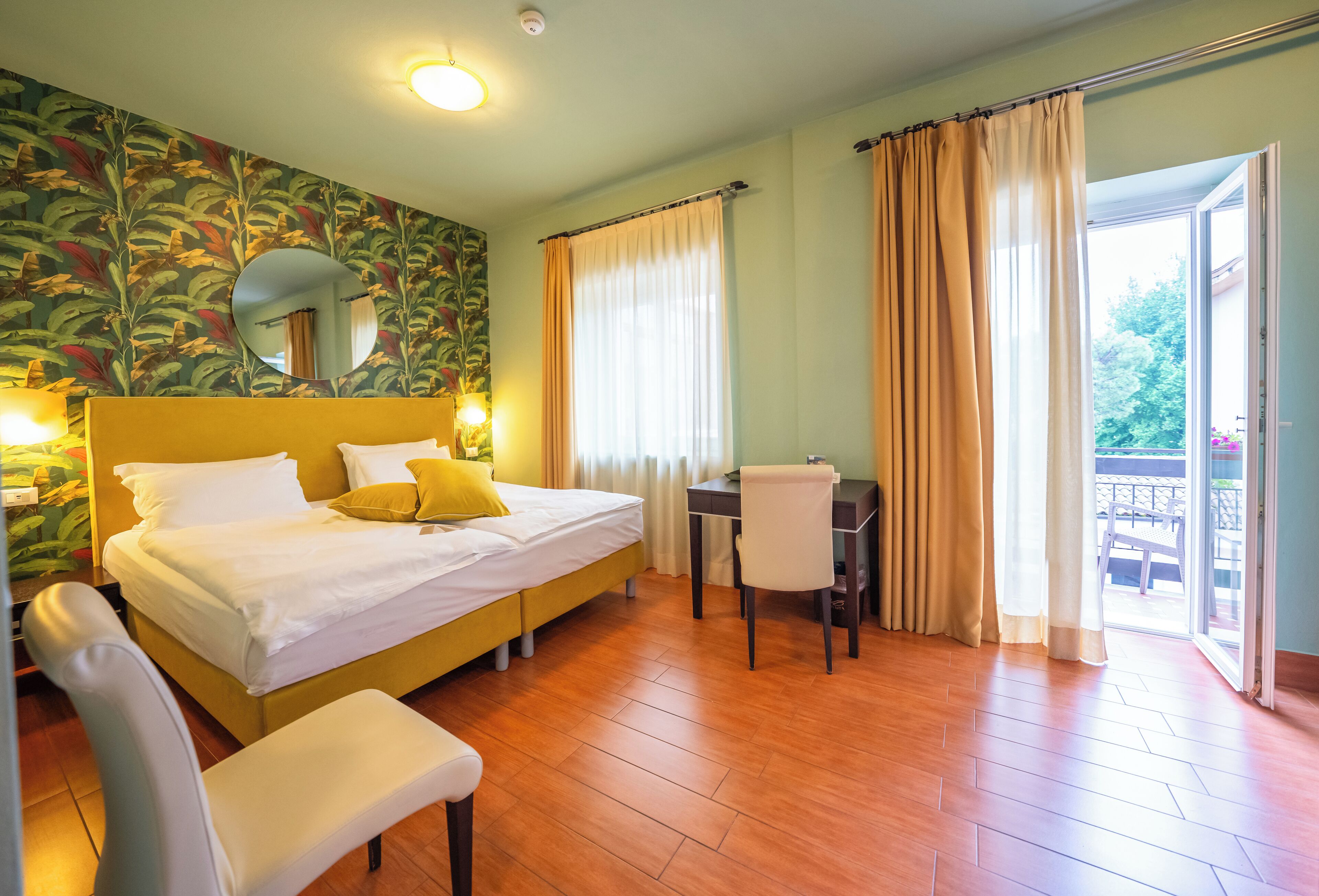 Habitación de hotel con cama, escritorio, silla y balcón con cortinas.