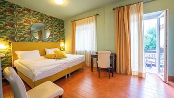 Habitación de hotel con cama, escritorio, silla y balcón con cortinas.